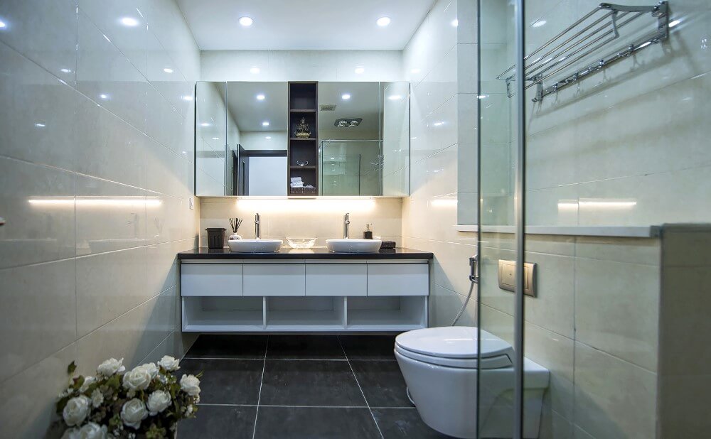Cải tạo sửa chữa nhà chung cư với phòng tắm bố trí nội thất với tấm gương trên bồn rửa bồn tắm chính là cánh cửa mở ra một khu vực lưu trữ kín đáo.