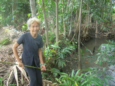 Bà Nguyễn Thị Nay bên đìa tôm đã bỏ hoang từ nhiều năm nay do nước rạch Bà Chèo bị ô nhiễm nặng